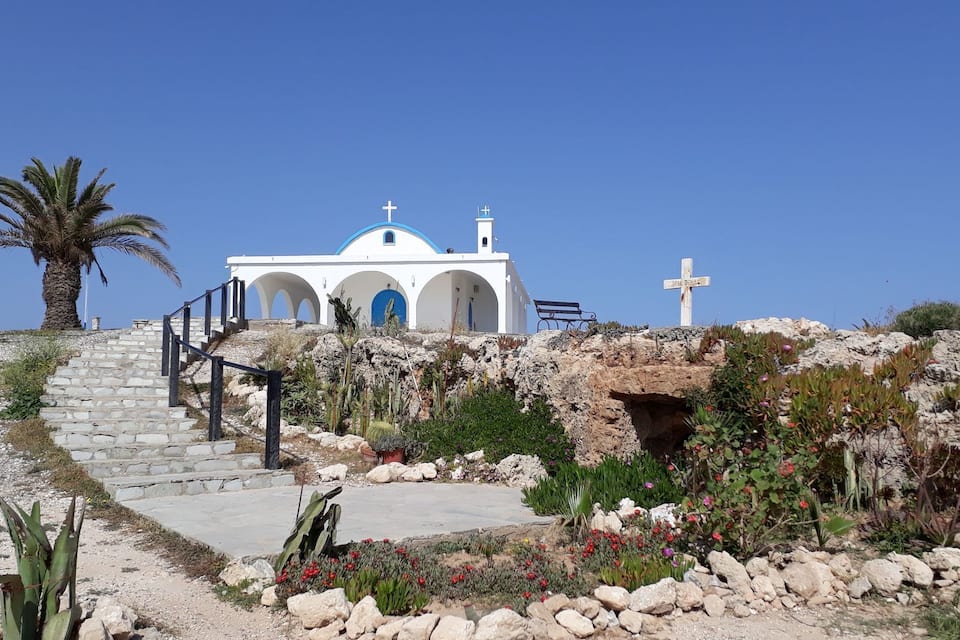 A white church with blue accents and a cross on a hill.
