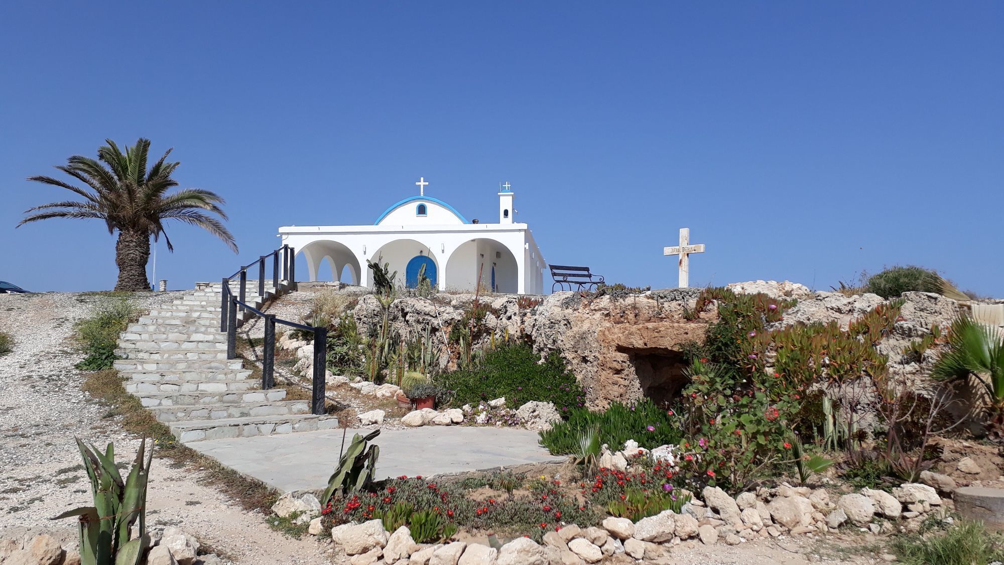 A white church with blue accents and a cross on a hill.