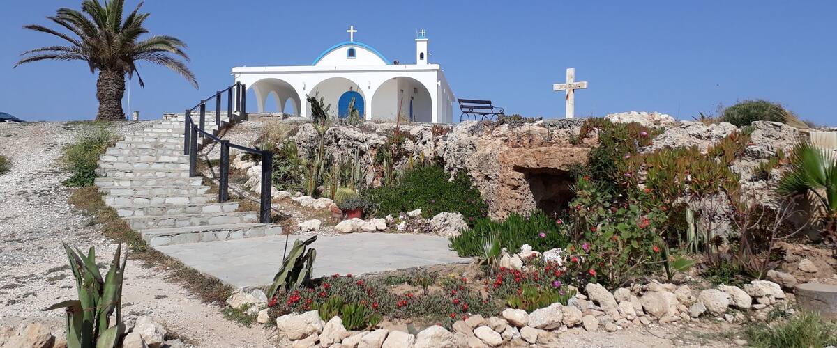 A white church with blue accents and a cross on a hill.
