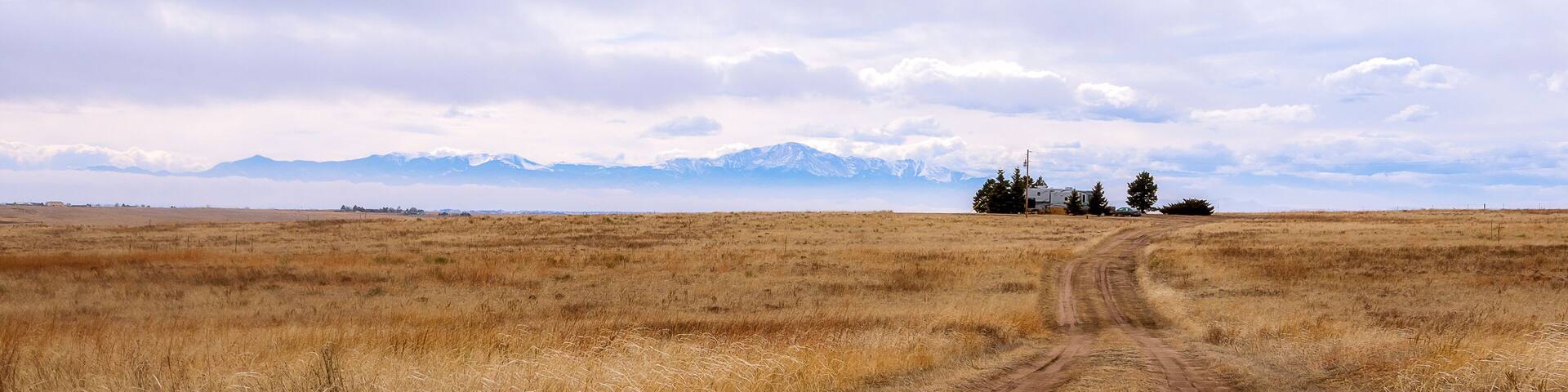 Beautiful Colorado landscape with a meadow, road, farm house, and famous Pikes Peak in the distance