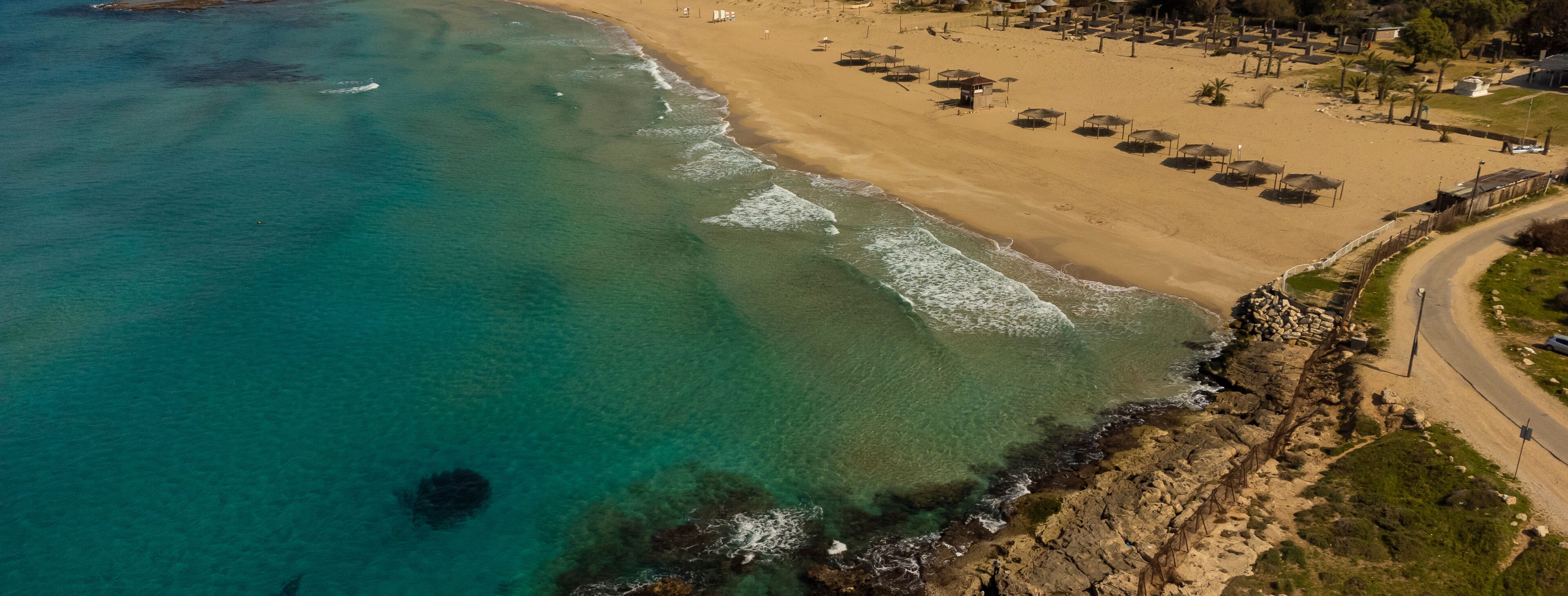 A coastal beach with clear turquoise waters, a sandy shore, and a rocky outcrop.