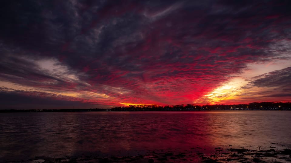 A sunset over a body of water with a dramatic red sky.