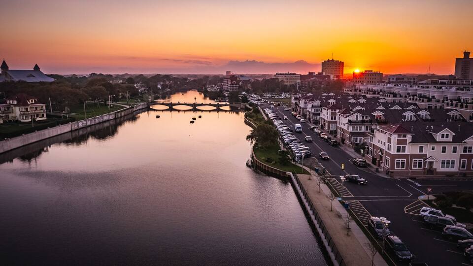 A river with bridges, a row of parked cars, and residential buildings during sunset.