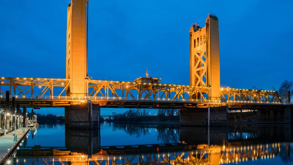 A bridge with two towers and a lit walkway, reflecting on the water below.