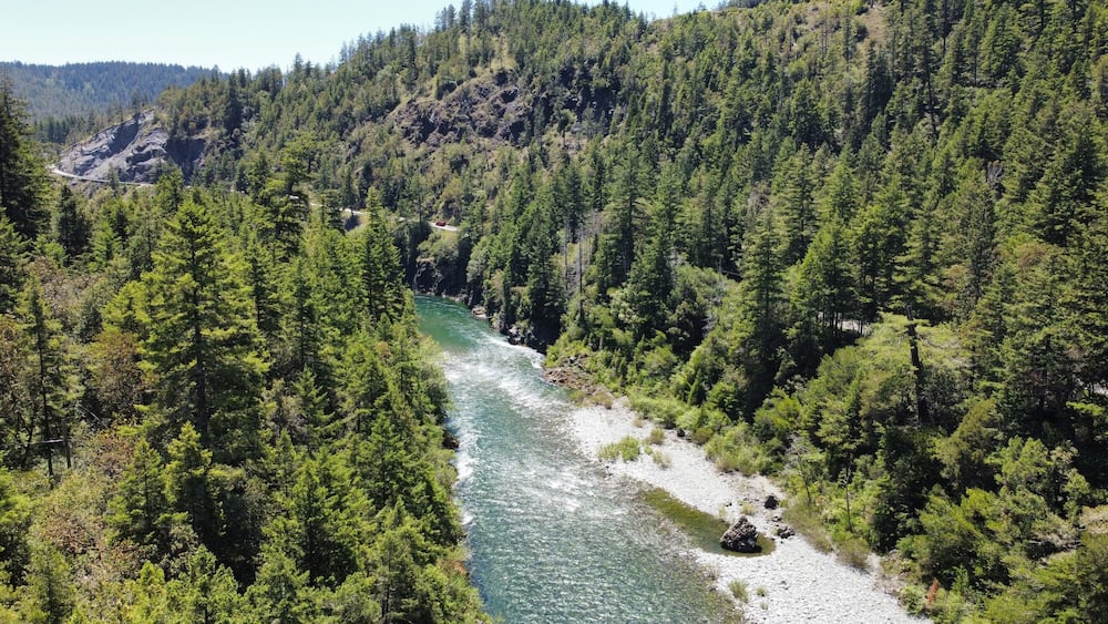 A river winding through a densely forested valley with rocky outcrops and a road curving along the river's edge.