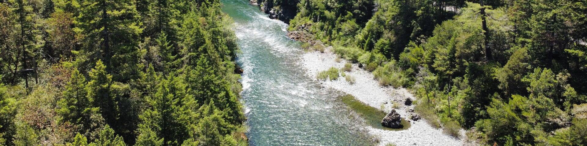 A river winding through a densely forested valley with rocky outcrops and a road curving along the river's edge.