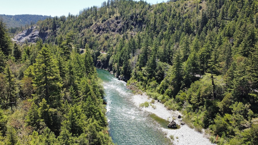 A river winding through a densely forested valley with rocky outcrops and a road curving along the river's edge.