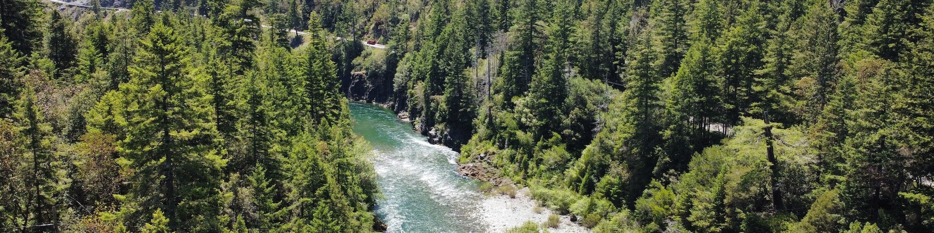 Un río serpentea por un valle densamente boscoso con afloramientos rocosos y una carretera que se curva a lo largo de la orilla.