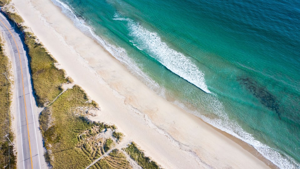 An aerial view of a beach with a road running parallel to the shoreline.