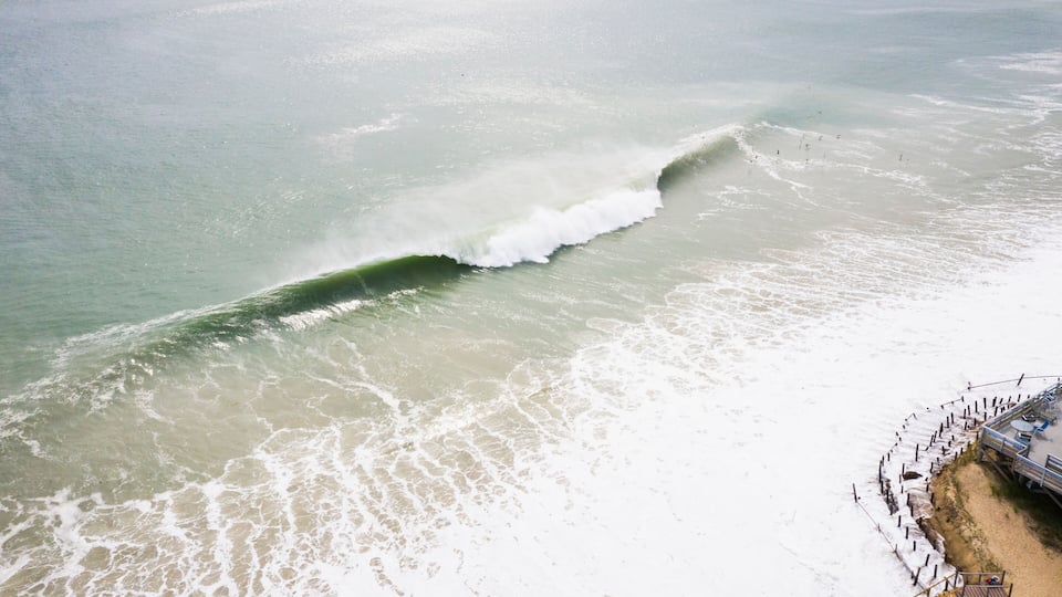 A beach with waves, a pier, and a sandy shore.
