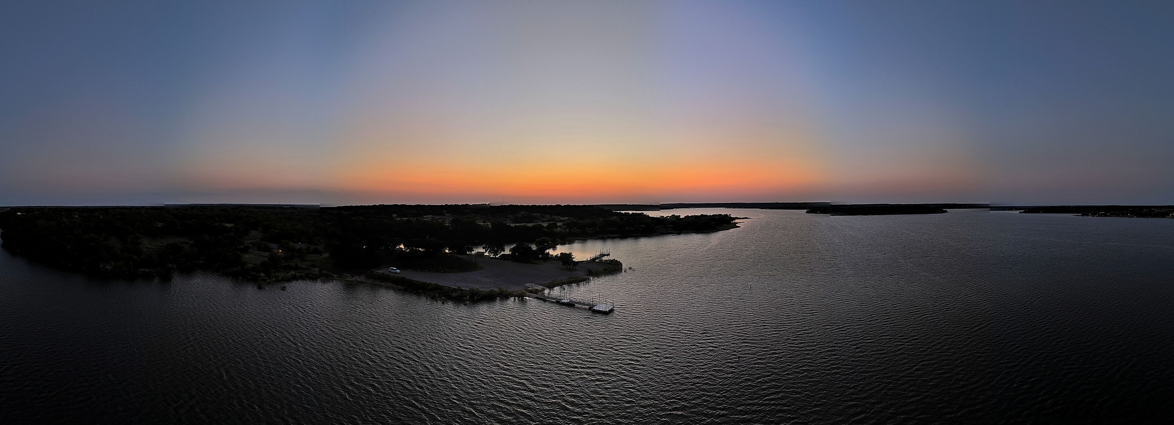 A sunset over a calm body of water with a small island and a dock.