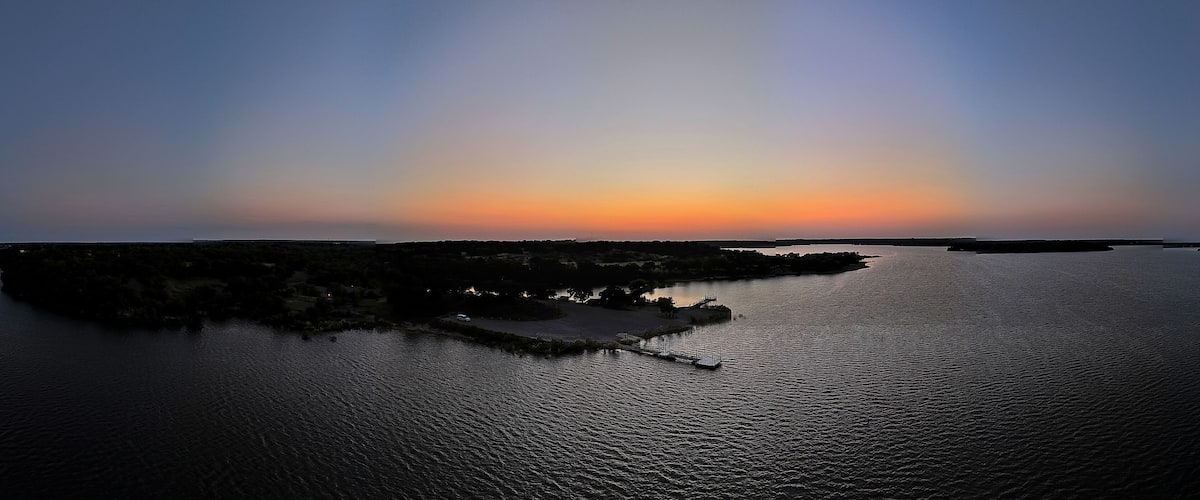 A sunset over a calm body of water with a small island and a dock.