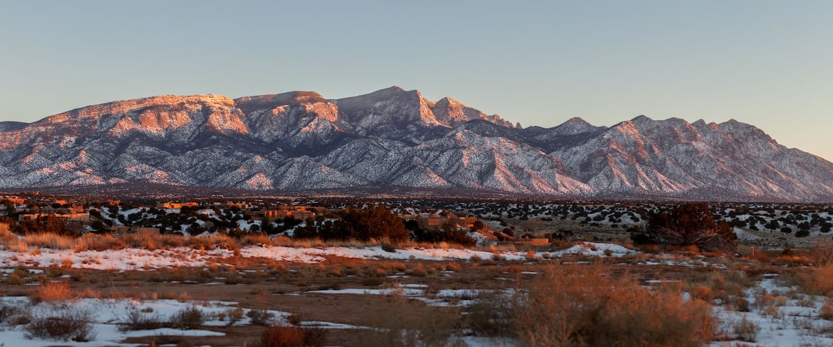 A mountain range with snow-covered peaks and a valley with sparse vegetation.