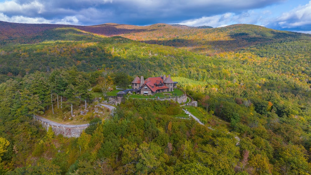 A large house surrounded by dense forest and rolling hills.