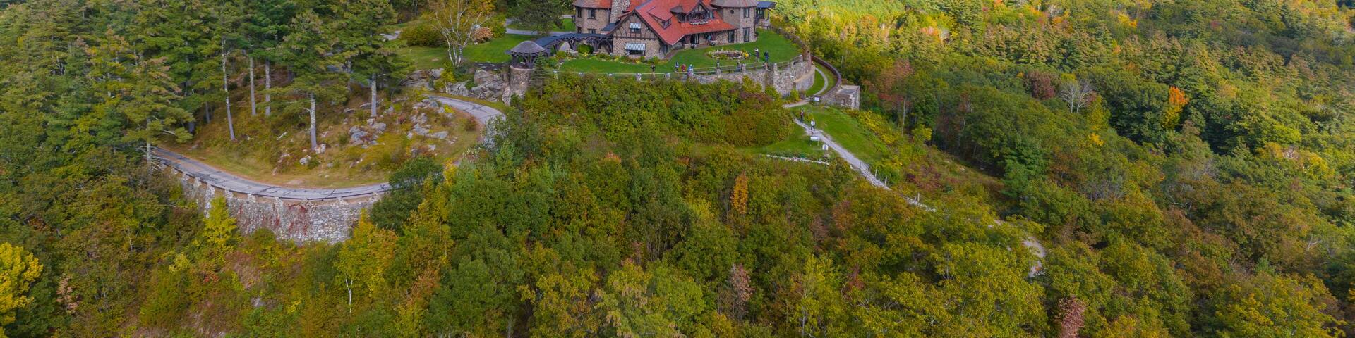 A large house surrounded by dense forest and rolling hills.