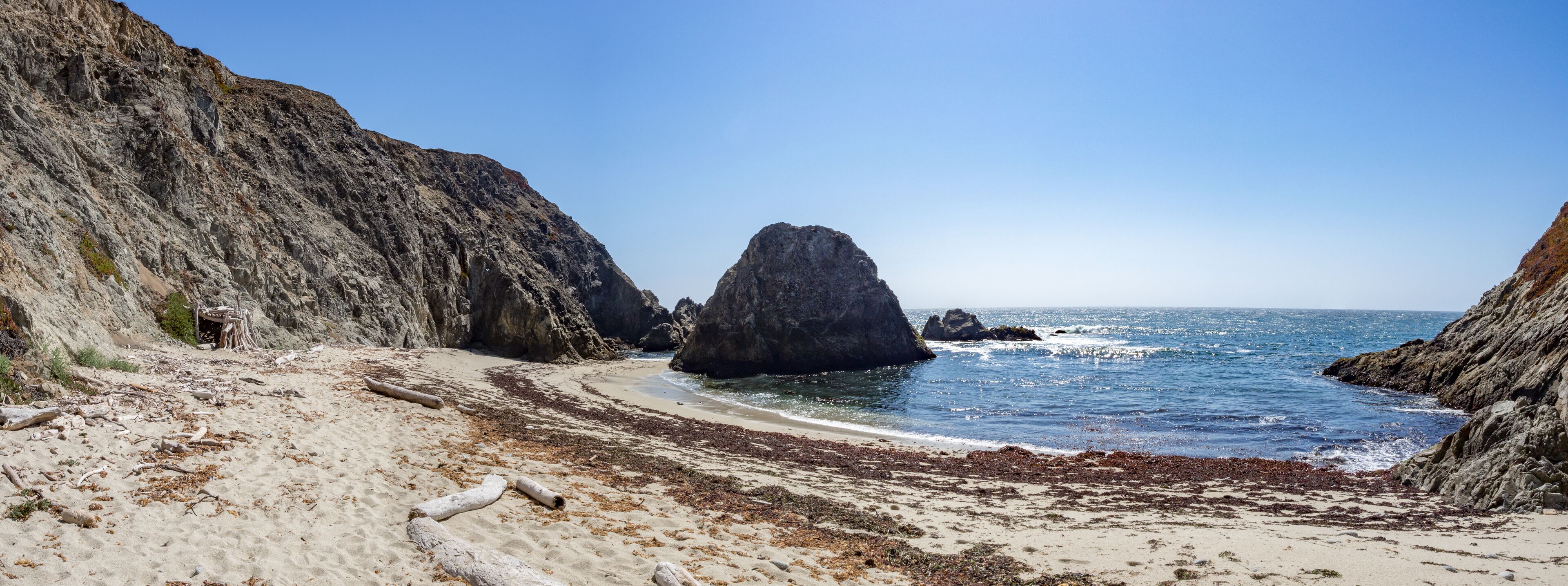 A rocky coastline with a prominent rock formation, sandy beach, and clear blue sea.