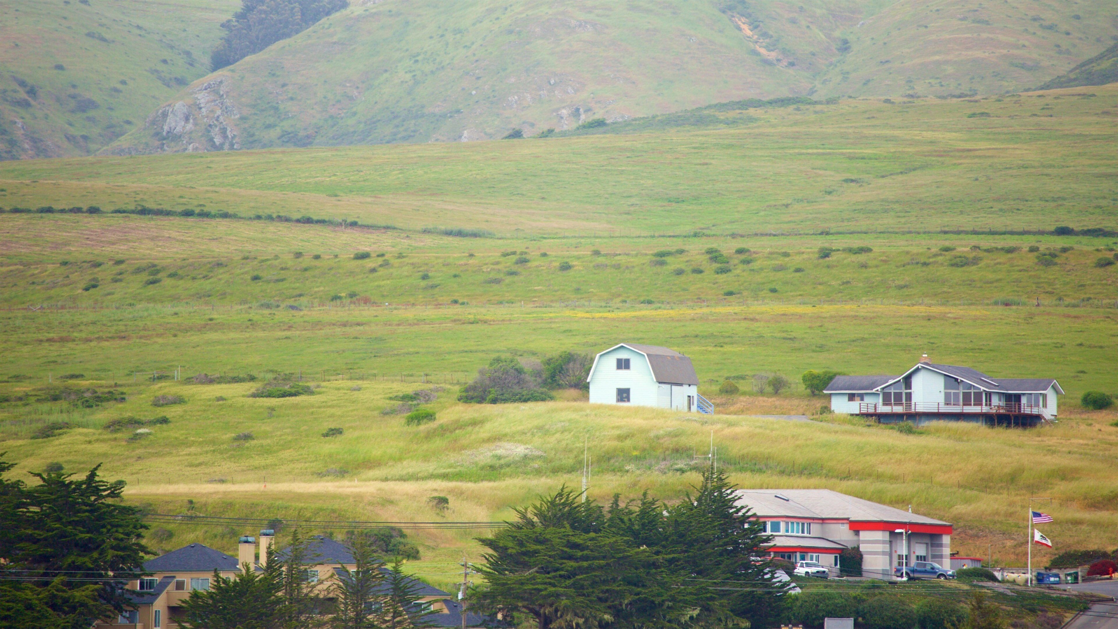 A rural landscape with rolling hills, a small white house, and a larger house with a porch.