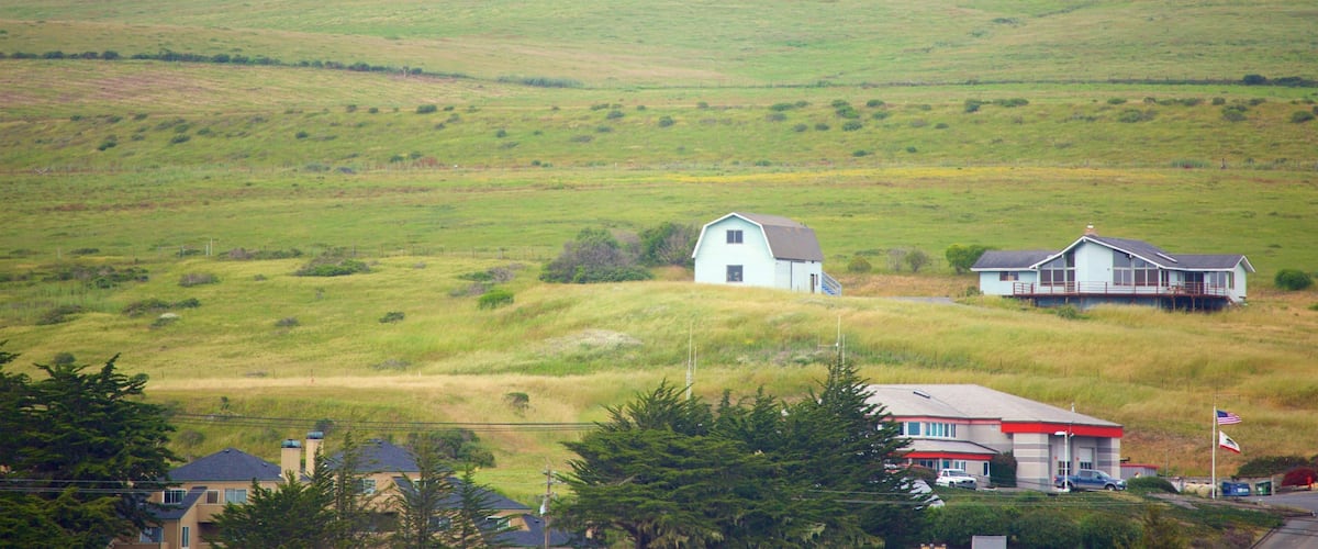 A rural landscape with rolling hills, a small white house, and a larger house with a porch.