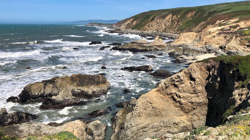 A rocky coastline with waves crashing against the shore and cliffs in the background.