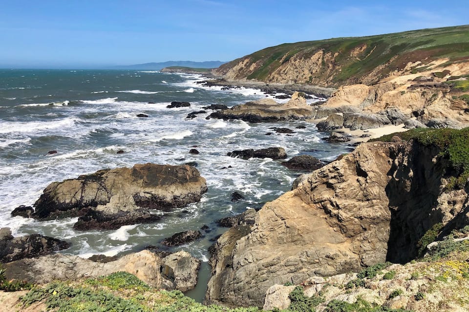 A rocky coastline with waves crashing against the shore and cliffs in the background.