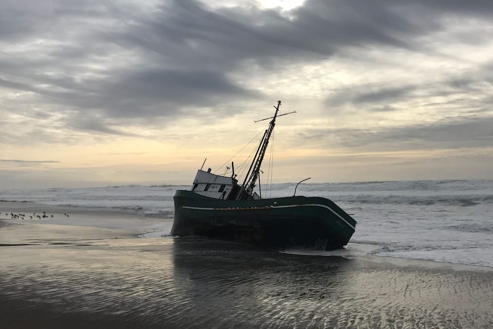 A green fishing boat stranded on a beach with rough sea waves and a cloudy sky.
