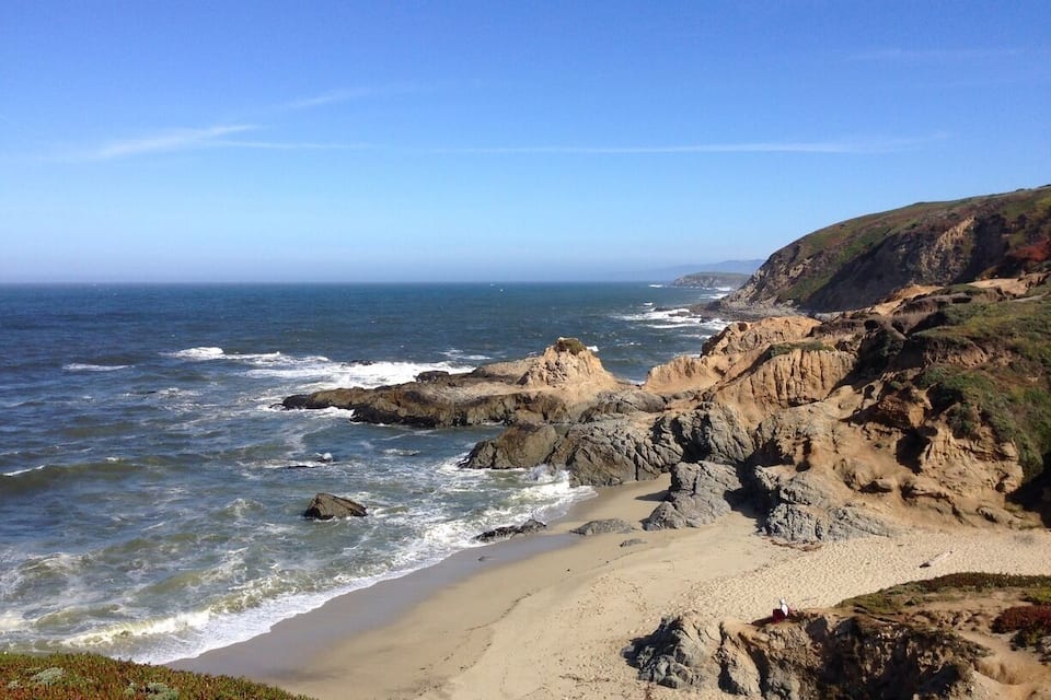 A coastal landscape with rocky cliffs, sandy beach, and the ocean.