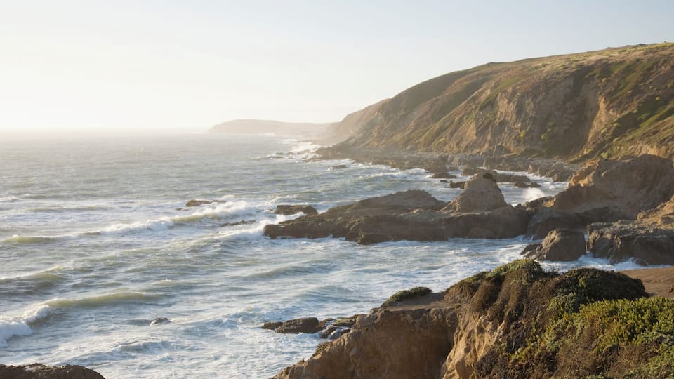 A coastal landscape with rocky cliffs and waves crashing against them.