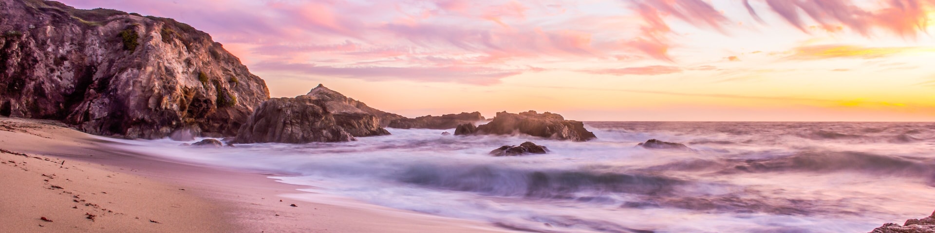 Una playa con arena fina, afloramientos rocosos y un cielo al atardecer.