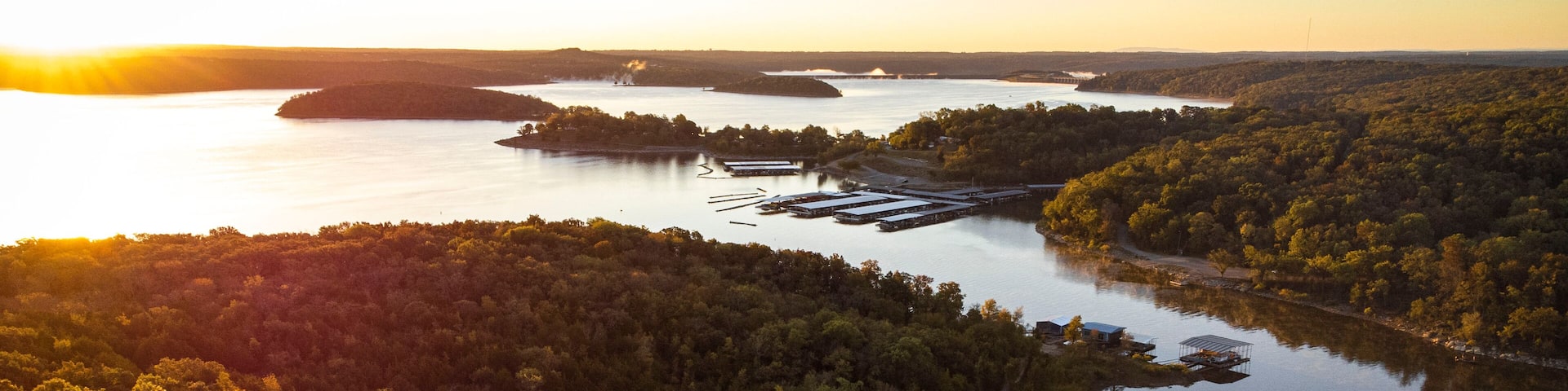 A river winding through a densely forested landscape with a small dock and buildings along the shore.