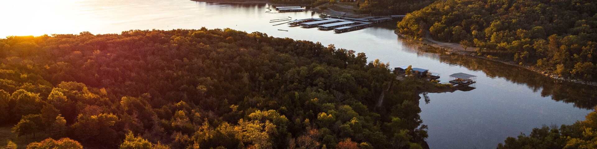 A river winding through a densely forested landscape with a small dock and buildings along the shore.