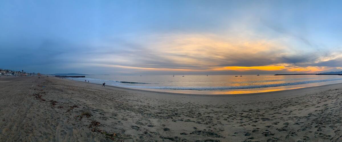 A beach with footprints, a calm sea, and a sunset sky.