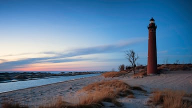 Un faro rojo en una playa arenosa con poca hierba y un cielo despejado.