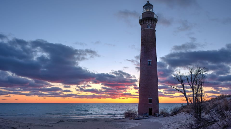 A tall brick lighthouse by the ocean at sunset.