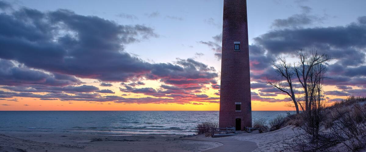 A tall brick lighthouse by the ocean at sunset.