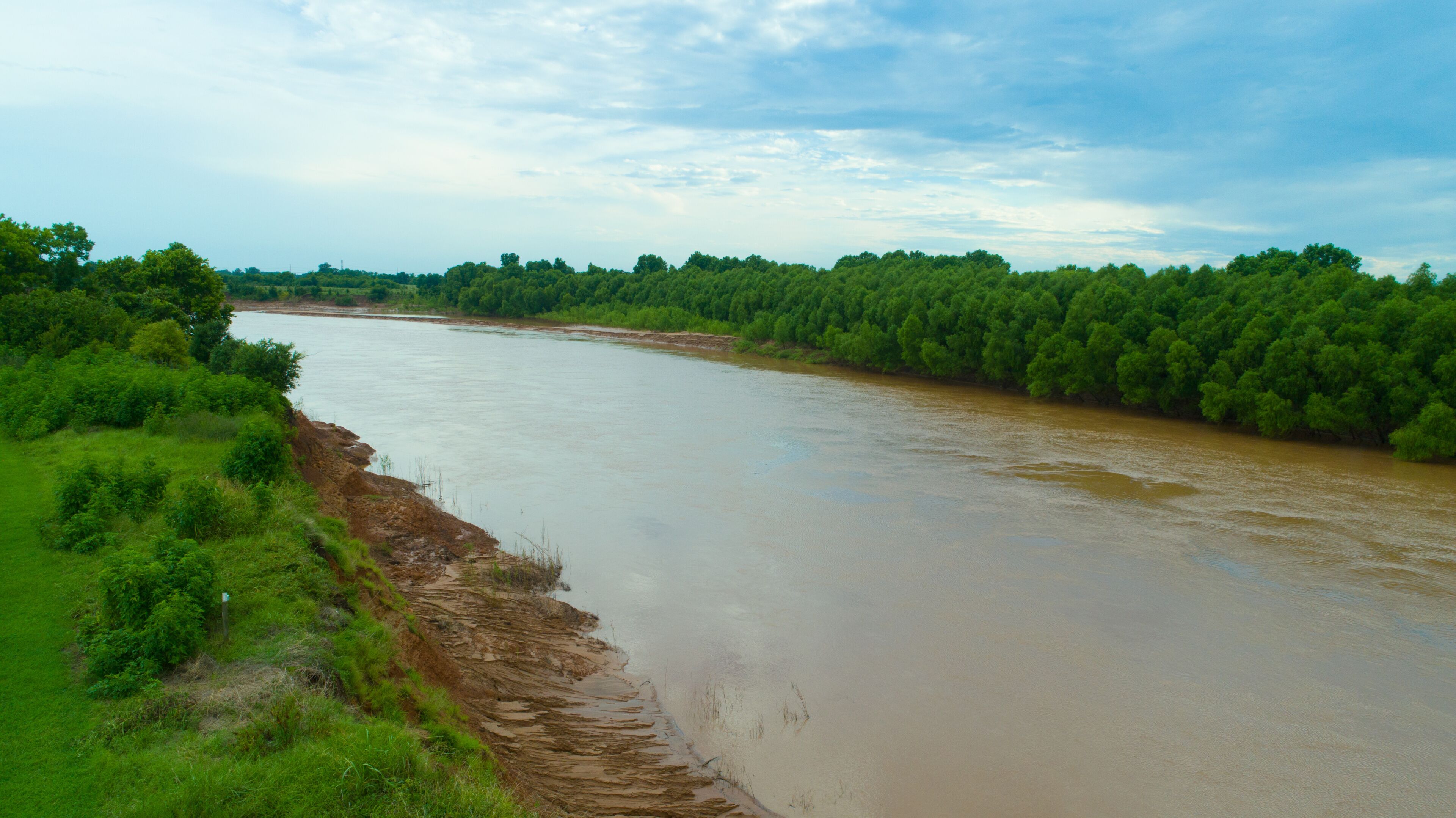 A river flowing through a green landscape with dense trees on both sides.