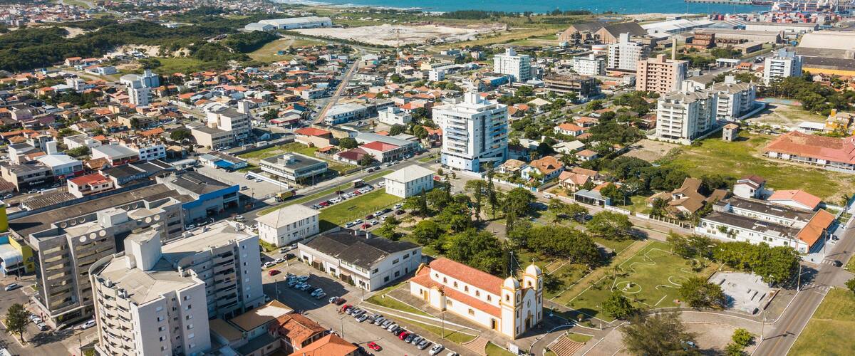 A coastal cityscape with dense urban development, a prominent church, and a port with shipping containers.