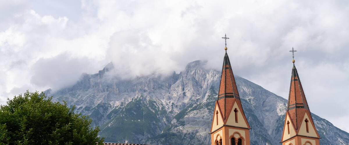 A church with two spires, a mountain in the background, and clouds partially covering the peak.