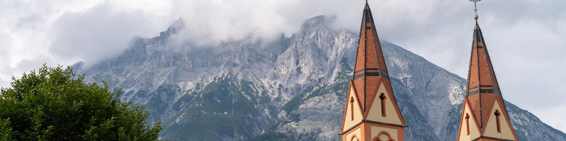 A church with two spires, a mountain in the background, and clouds partially covering the peak.