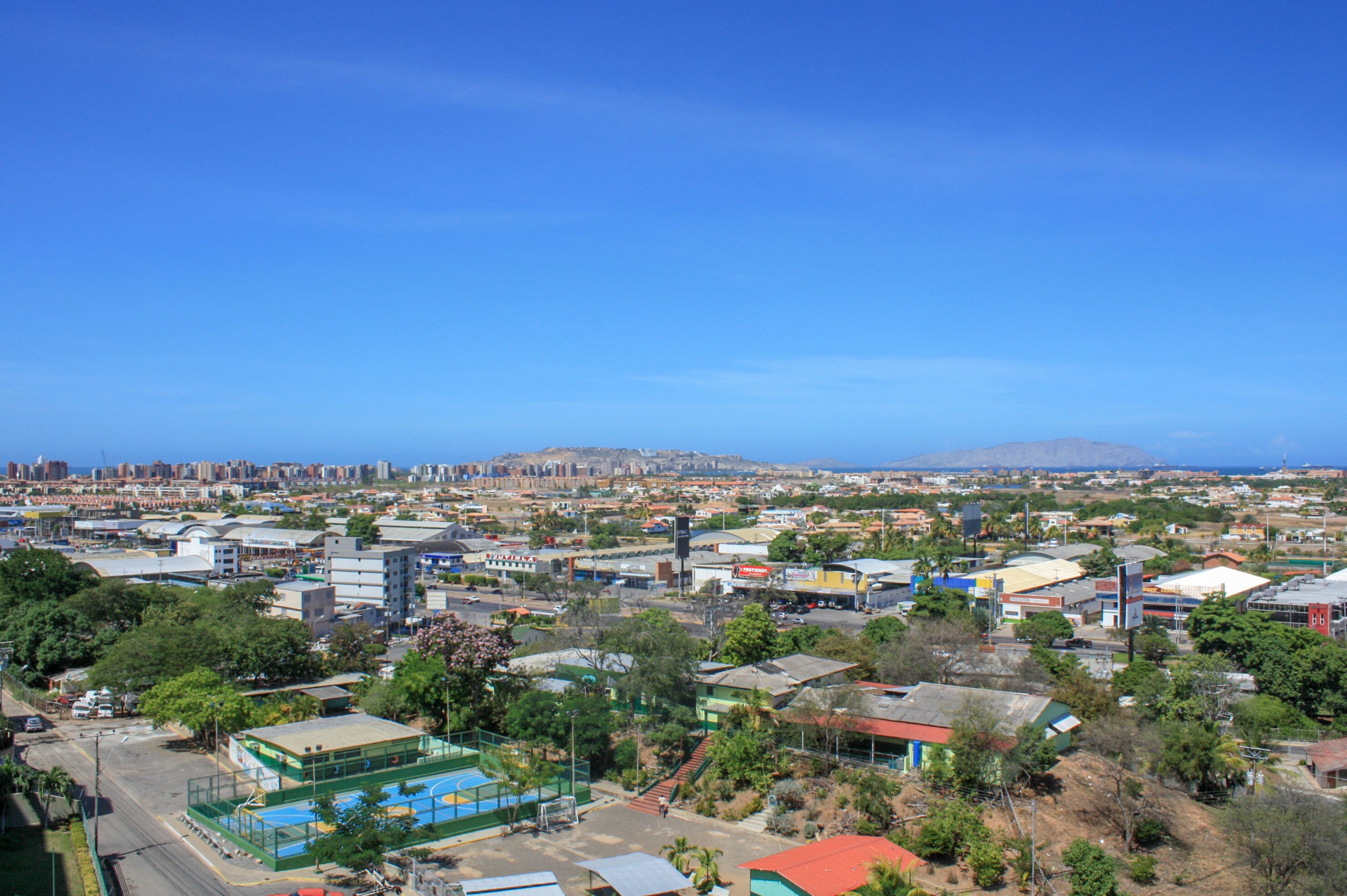 A cityscape with a clear blue sky, a mix of residential and commercial buildings, and a distant mountain range.