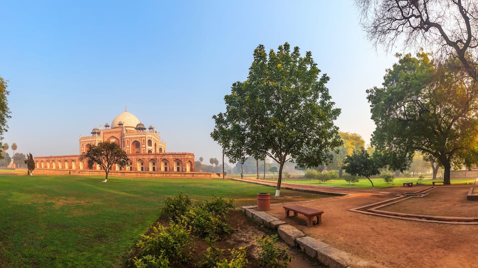 A large, historic building with a dome, surrounded by a park with trees and pathways.