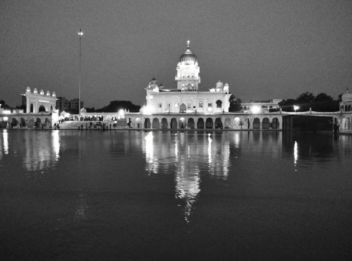 Un edificio imponente con una gran cúpula y ventanas arqueadas, reflejado en una superficie acuática tranquila por la noche.