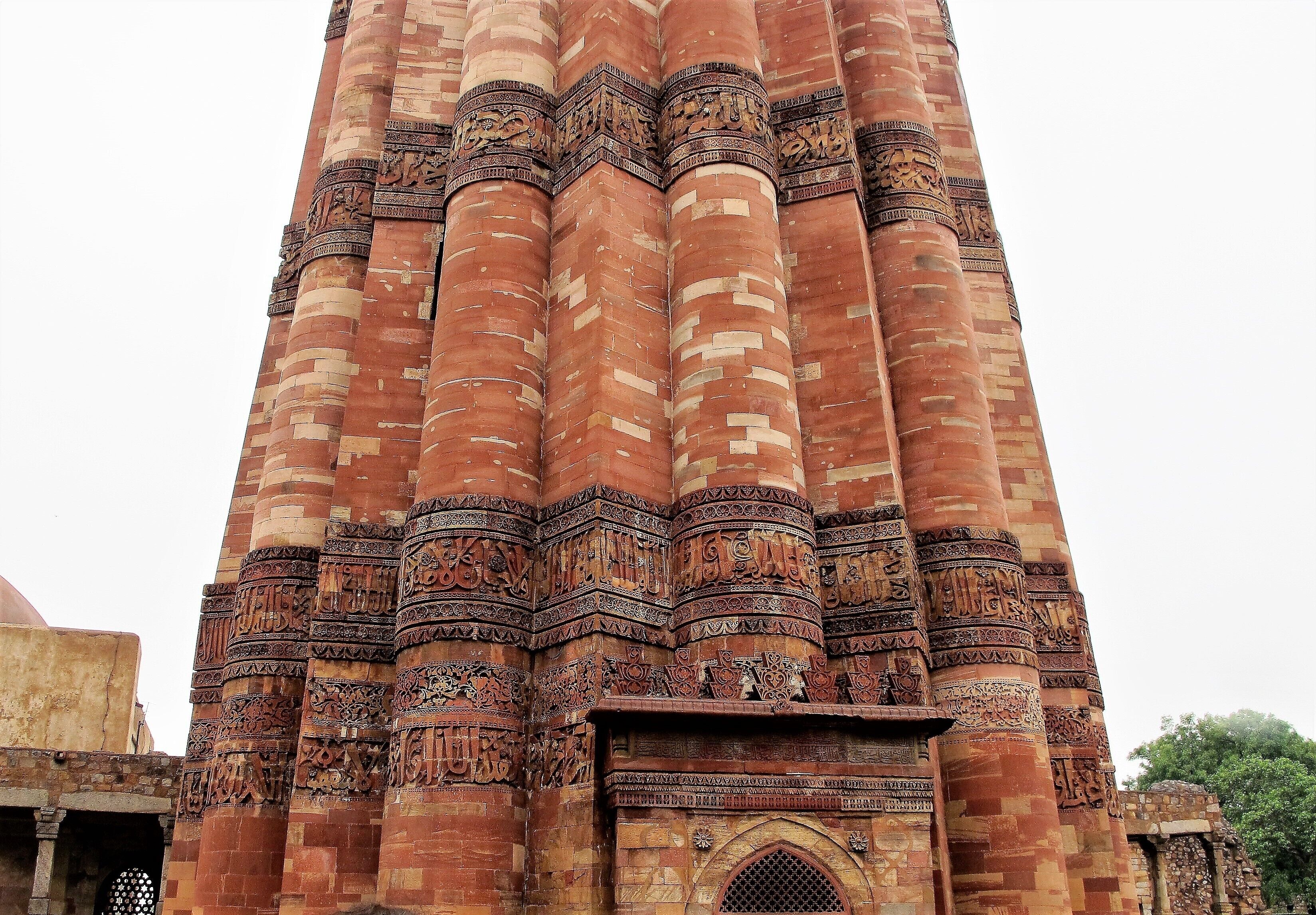 Verses from the holy Quran are carved on the sandstone walls of the Qutub Minar. #Details
A world heritage site, the Qutub Minar is a tall conical minaret, five stories tall with 379 steps to the top. It was built by the first Muslim ruler of Delhi Qutuab-ud-Aibak and construction began in 1200 AD but completed by his successors in the late 1300s. Hence each level shows different architectural styles. The first three storeys are made of red sandstone; the fourth and fifth storeys are of marble and sandstone. 
The tower is closed to the public but one can enjoy the exquisite carvings on the outside that reflect Indo-Islamic Afghan architecture. There is a lot to see in the Qutub complex including a mosque and an iron pillar of Delhi. 
