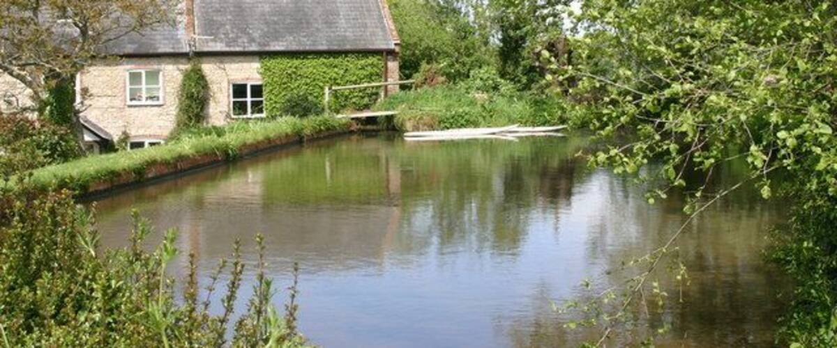 A calm river with a stone house and greenery.