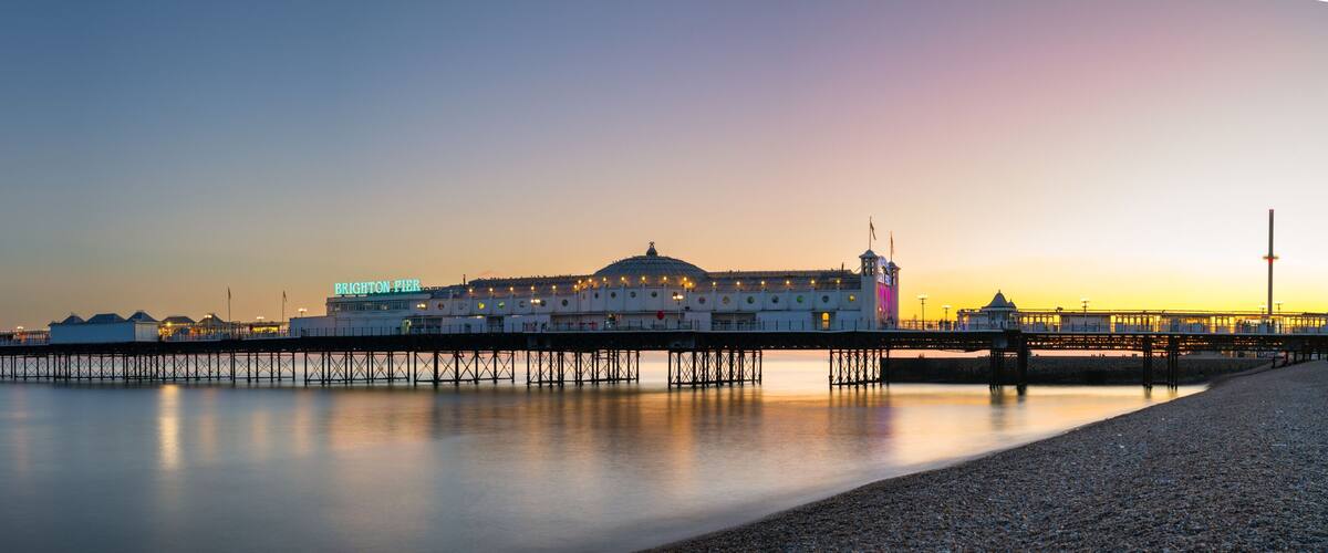 A pier extending into calm waters with a large building labeled 'BRIGHTON PIER' and a dome structure in the background.