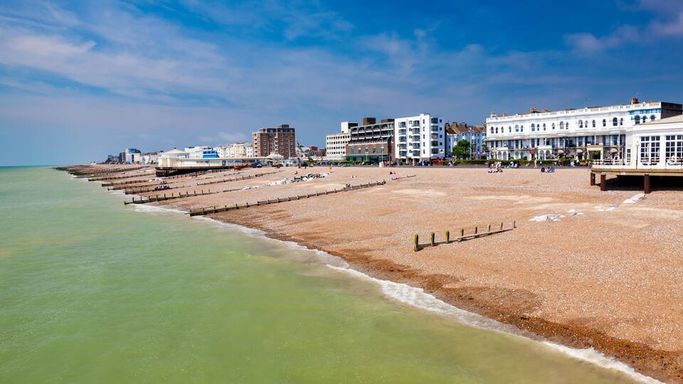 A beach with a wooden promenade, buildings, and a clear sky.