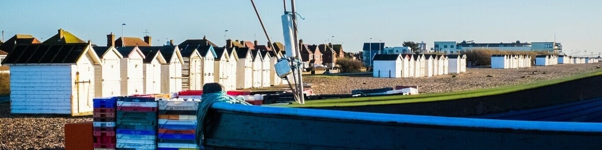 Um barco numa praia de seixos com uma fileira de cabanas de praia ao fundo.