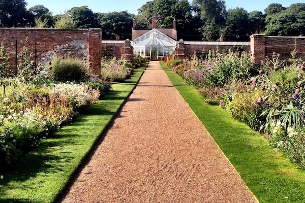 A garden pathway leading to a conservatory with brick walls and lush greenery.