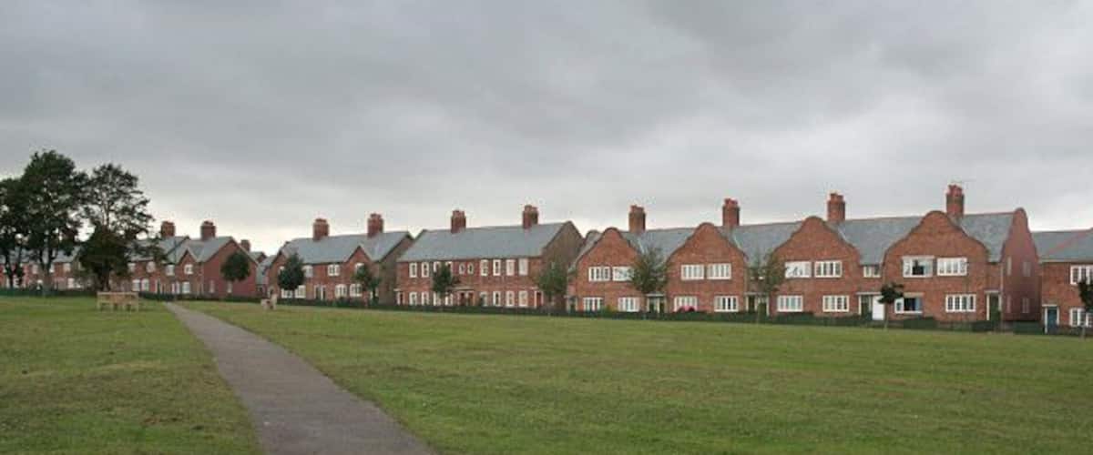A row of red brick houses with a paved path leading through a grassy field.