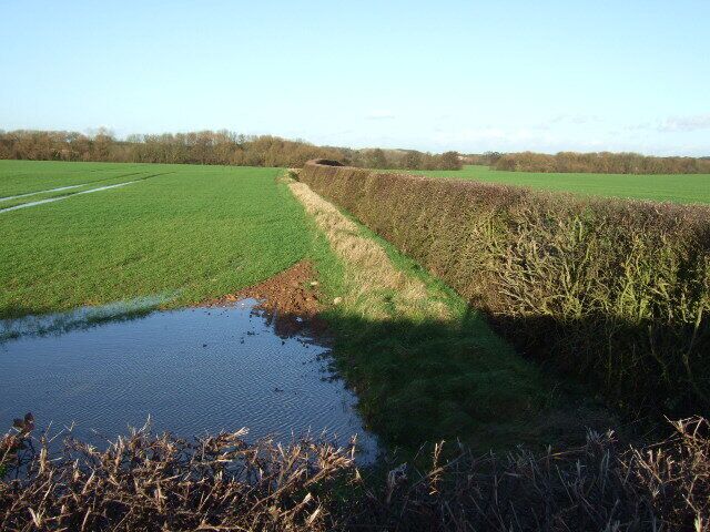 A rural landscape with a field, a ditch, and a water body.