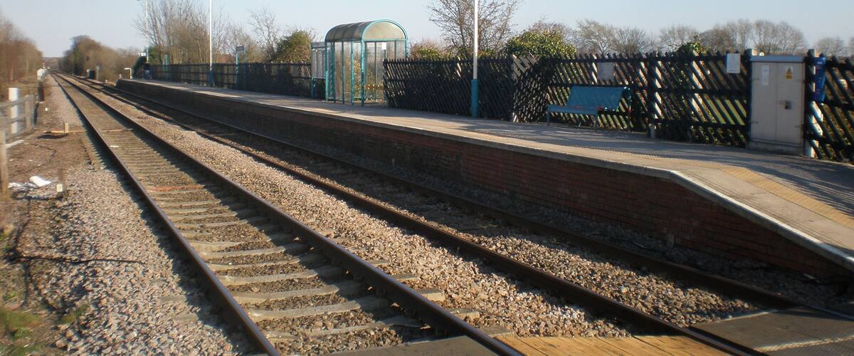 A railway station platform with tracks, a shelter, and a fence.